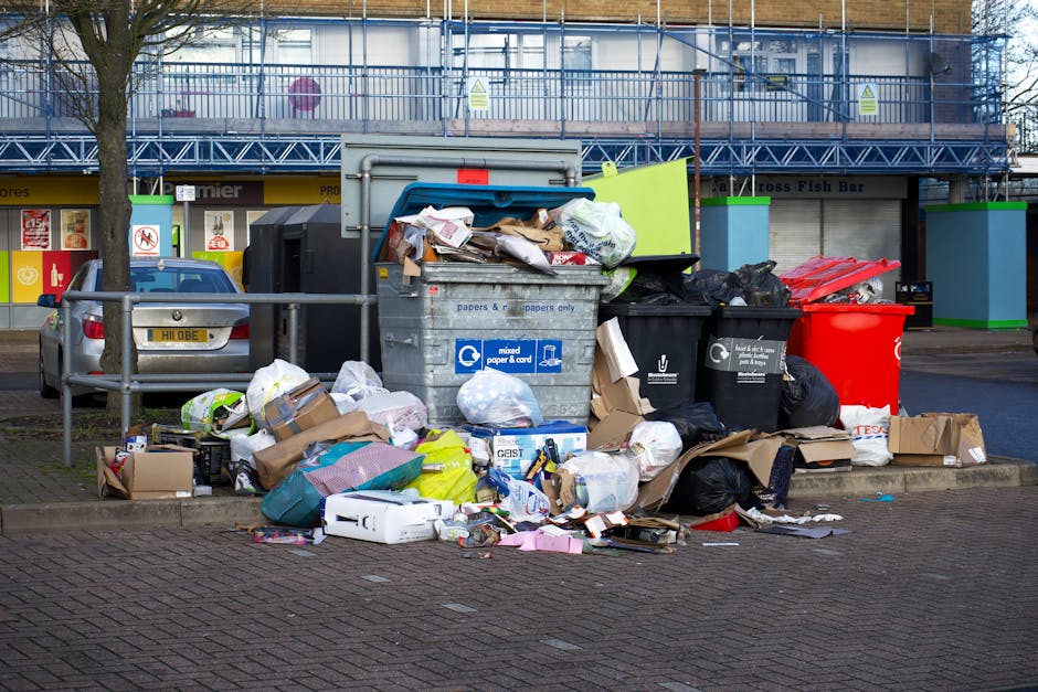 A group of large white plastic bags filled with various types of waste, tightly knotted at the top with orange ties, are placed outdoors on a paved surface. The bags appear full and are slightly trans